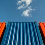 Kontainer pengiriman berwarna merah dan biru di area pelabuhan logistik